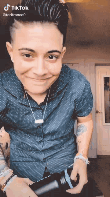a man with a shaved head is smiling and holding a camera with tiktok written on the bottom right