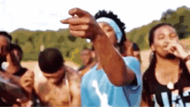a man in a blue shirt is pointing at something in front of a crowd .