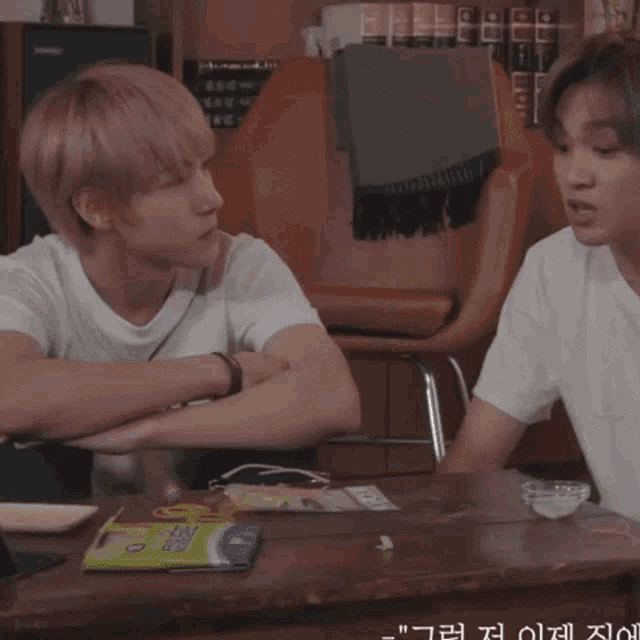 two young men are sitting at a table and one has a circle on his shirt that says ' yo ' on it
