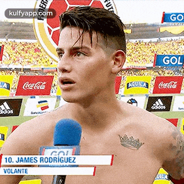 a shirtless man with a tattoo on his chest is talking into a microphone on a soccer field .