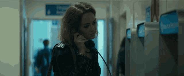 a woman is talking on a pay phone in a hallway with a blue exit sign in the background