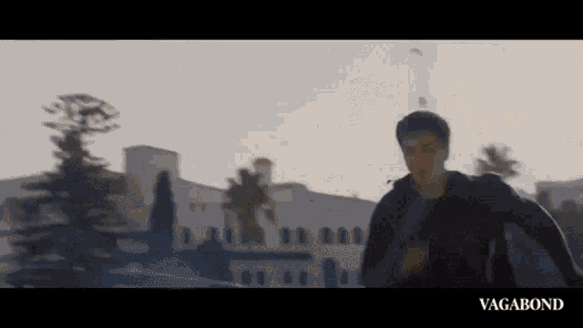 a man in a black jacket is running in front of a building with trees in the background .