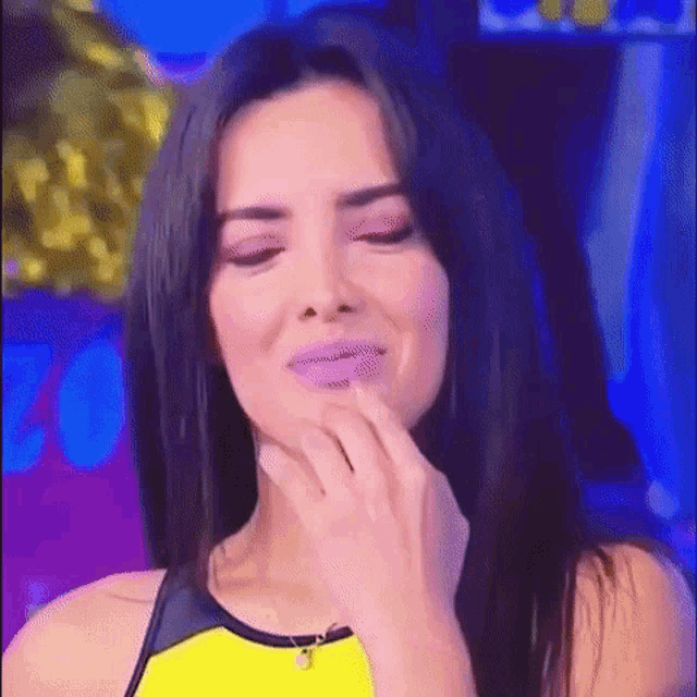 a woman in a yellow tank top is touching her face with her hand .