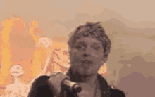 a man is singing into a microphone in front of a painting of a fire .