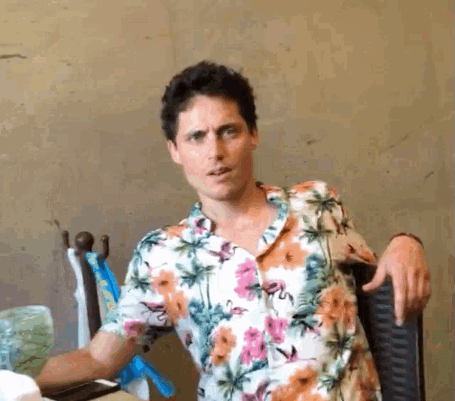 a man in a floral shirt sits in a chair