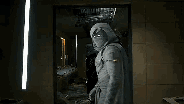 a man in a hooded jacket with glowing eyes is standing in front of a mirror in a dark room .