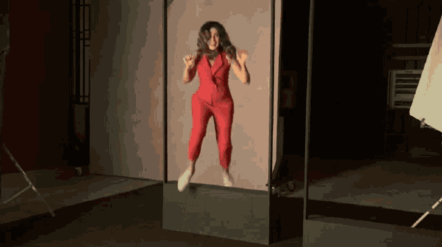 a woman in a red jumpsuit is jumping in the air in a dark room