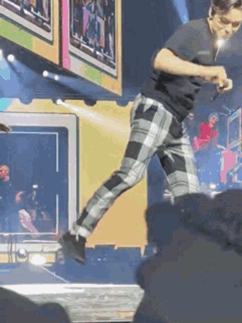 a man in plaid pants is standing on a stage with a microphone in his hand .