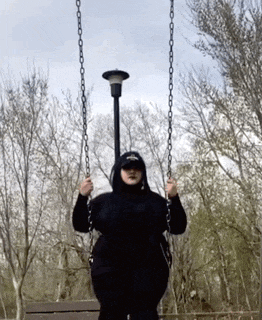a person wearing a black hoodie and a hat is swinging on a chain