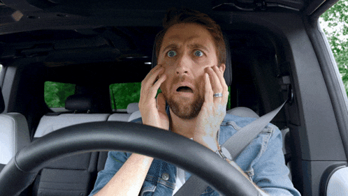 a man in a car with his hands on his face and a surprised look on his face