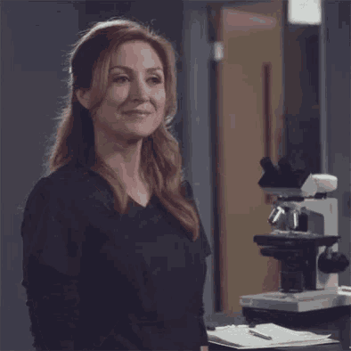 a woman is making a peace sign in front of a microscope .