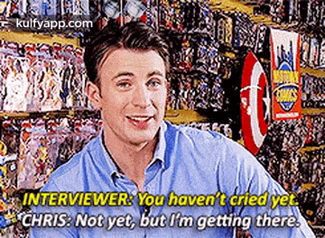 a man in a blue shirt is sitting in front of a wall of comics and talking to an interviewer .