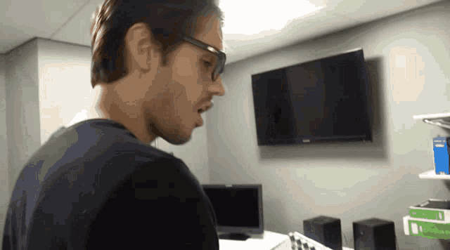 a man wearing glasses is standing in front of a monitor
