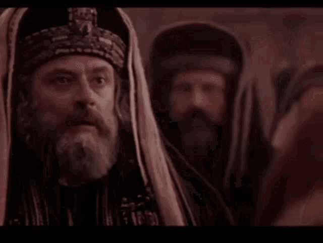 a man with a beard is standing in front of a group of men and screaming .