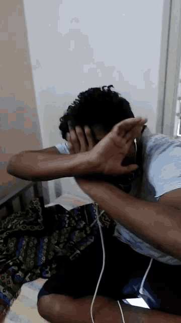 a man covering his face with his hands while wearing ear buds
