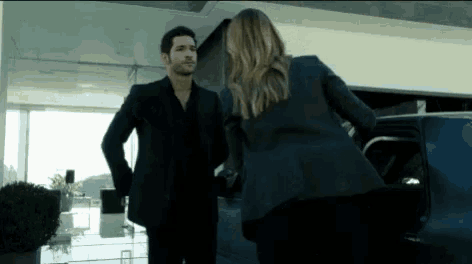 a man in a suit and a woman in a suit are standing next to each other in front of a car .
