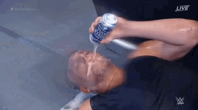a man is drinking from a can of beer while laying on the floor .