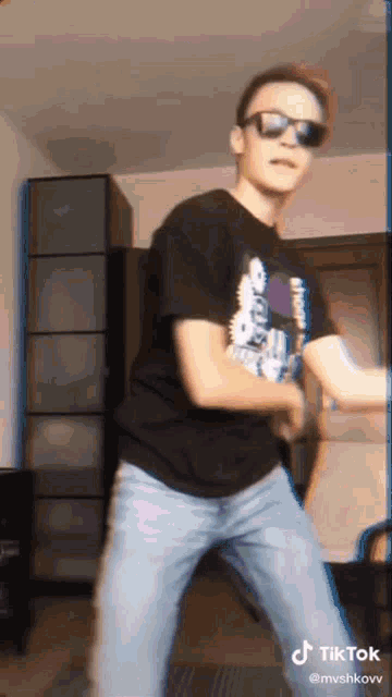 a man wearing sunglasses and a black shirt is dancing in a living room .