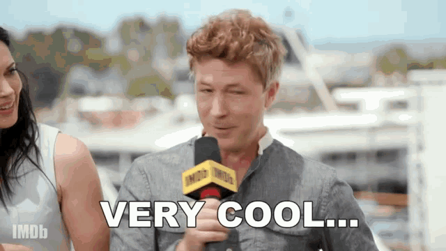 a man speaking into a microphone with the words very cool behind him