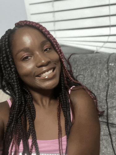 a woman with braids and a pink tank top smiles for the camera