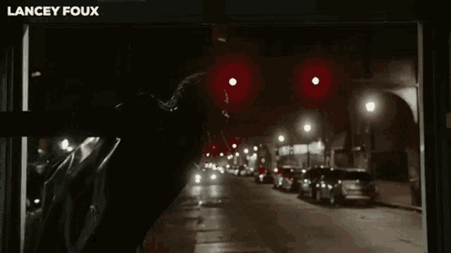 a man in a black jacket is standing in front of a red light with lancey foux written on the bottom right