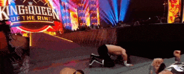 a wrestler is kneeling on the ground in front of a sign that says king queen of the ring .