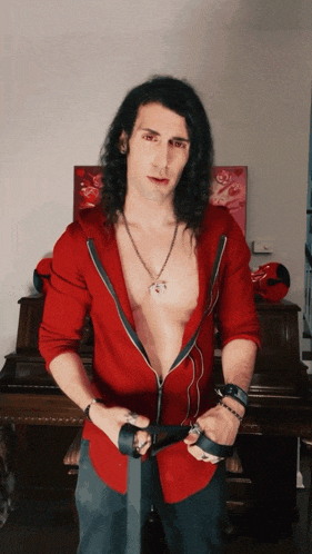 a man with long hair is standing in front of a piano wearing a red jacket