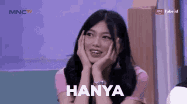 a woman is smiling with her hands on her face and the word hanya is on the screen behind her .
