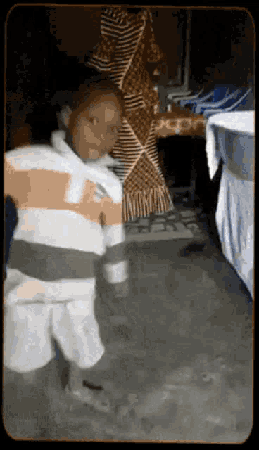 a young boy in a striped shirt and shorts is standing in a room .
