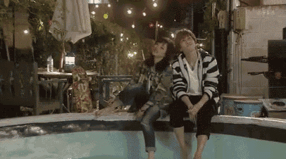 a man and woman are sitting on the edge of a pool .