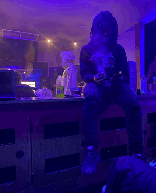 a man is sitting on a counter smoking a cigarette and looking at his phone