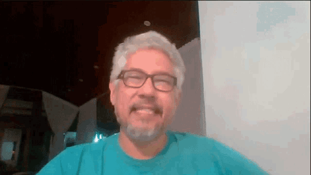 a man with glasses and a beard is smiling and wearing a blue shirt