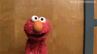 elmo from sesame street is sitting in front of a wooden door and smiling .