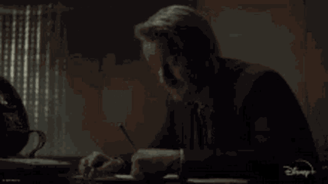 a man in a suit is sitting at a desk writing on a piece of paper .