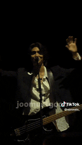 a man in a suit is playing a guitar in front of a microphone in a dark room with tiktok written on the bottom