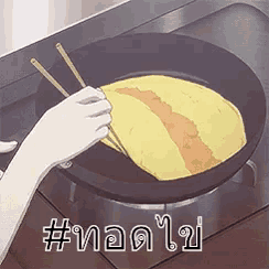 a person is cooking food in a frying pan with chopsticks .