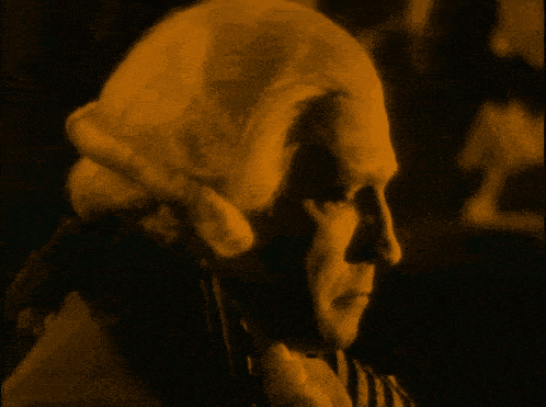 a man in a striped shirt is reading a piece of paper in a dark room