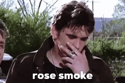 a man in a black jacket is smoking a cigarette with the words rose smoke above him