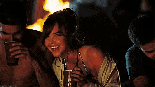 a woman in a bikini is smiling while holding a drink in front of a fire