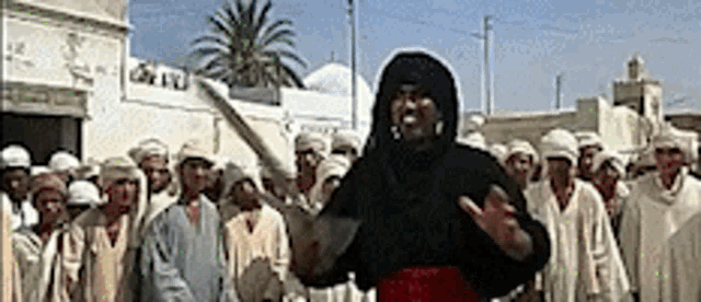 a man in a black hooded jacket is standing in front of a group of people .