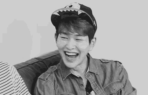 a black and white photo of a young man wearing a hat and laughing .