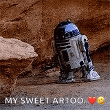 a r2d2 robot from star wars is standing in the dirt next to a rock .
