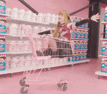 a woman is sitting in a pink shopping cart in a store