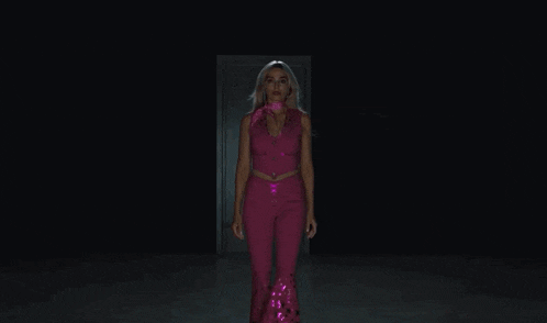 a woman in a pink outfit is standing in a dark room