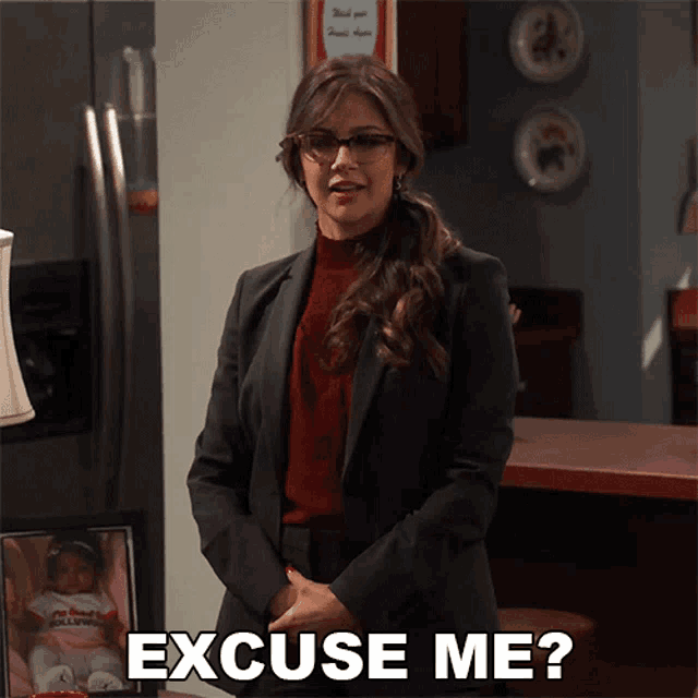 a woman in a suit stands in front of a refrigerator and says " excuse me "
