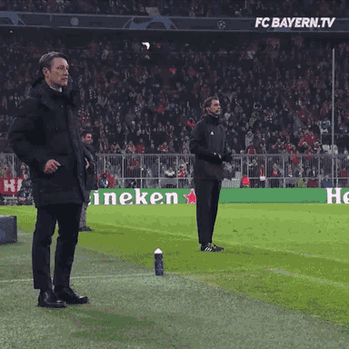 two men stand on a soccer field in front of a heineken ad