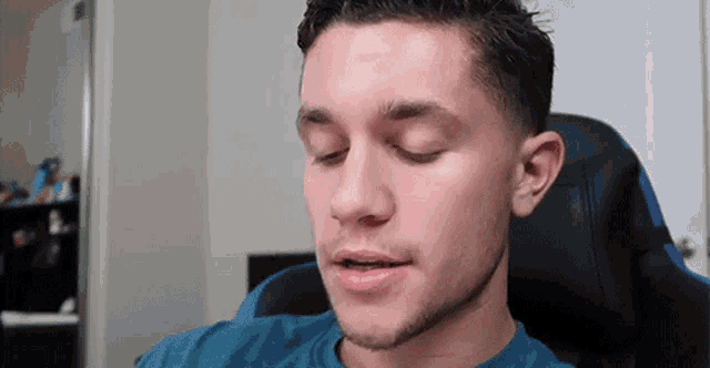 a man in a blue shirt is sitting in a chair with his eyes closed .