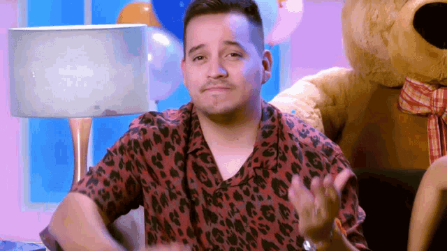 a man in a leopard print shirt is sitting next to a teddy bear