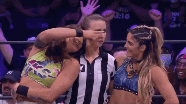 a female wrestler covering her eyes with her hand while standing next to another wrestler and a referee