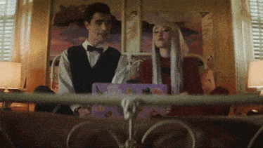 a man in a bow tie stands next to a woman with long white hair